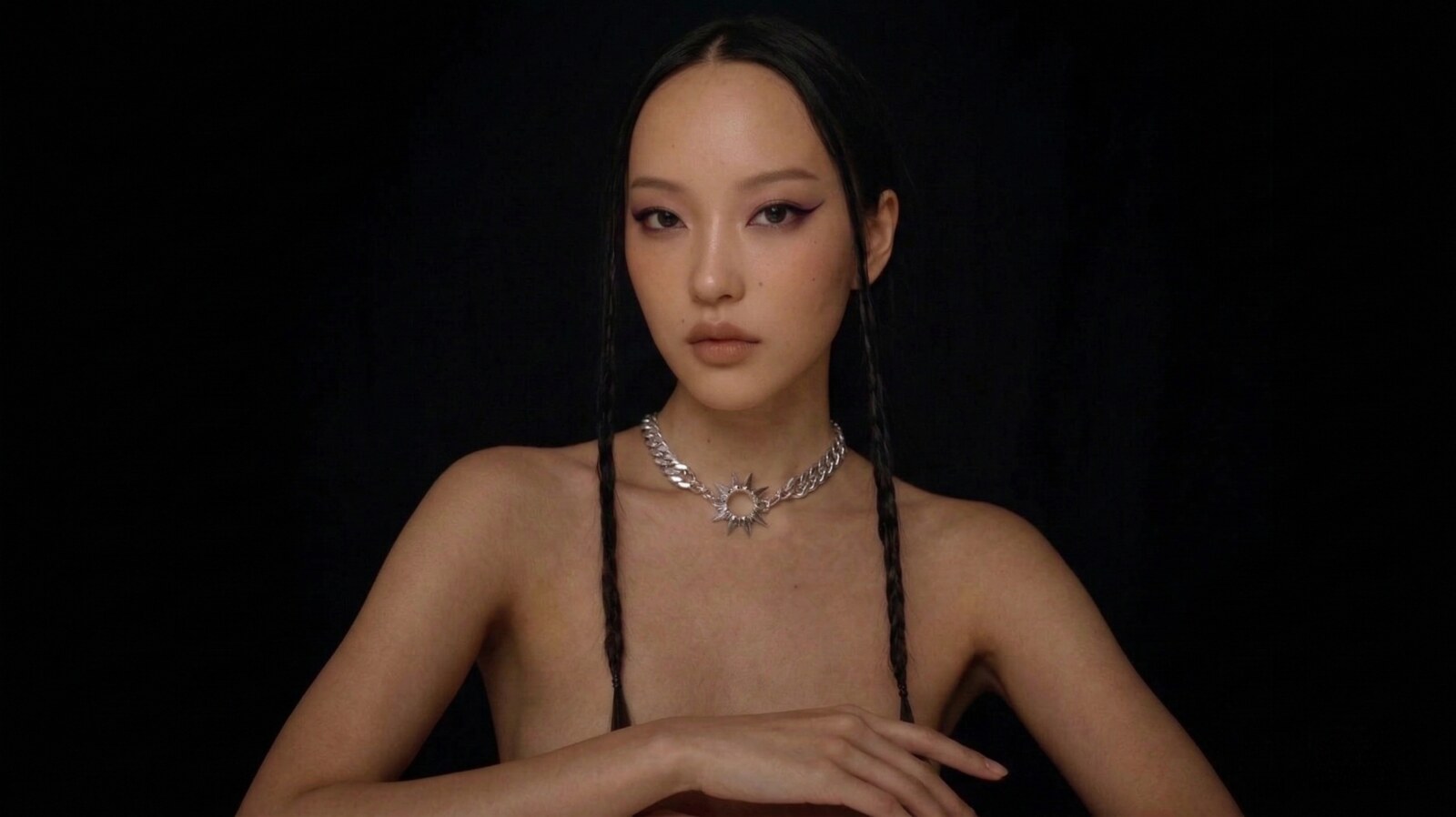 illi Collection Apex Necklace editorial hero portrait — East Asian model with braided hair and silver sunburst pendant on solid black